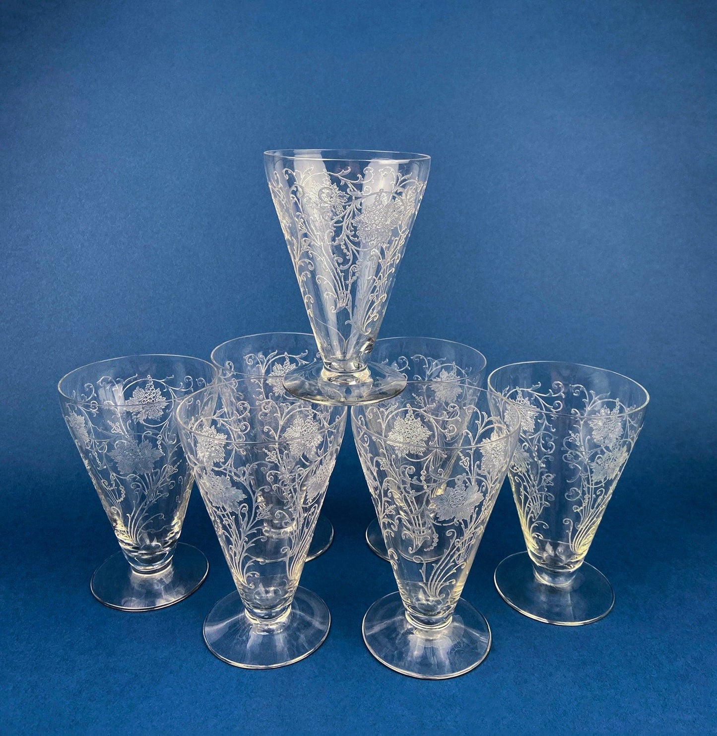 Set of six clear glass tumblers with floral engravings on a blue background