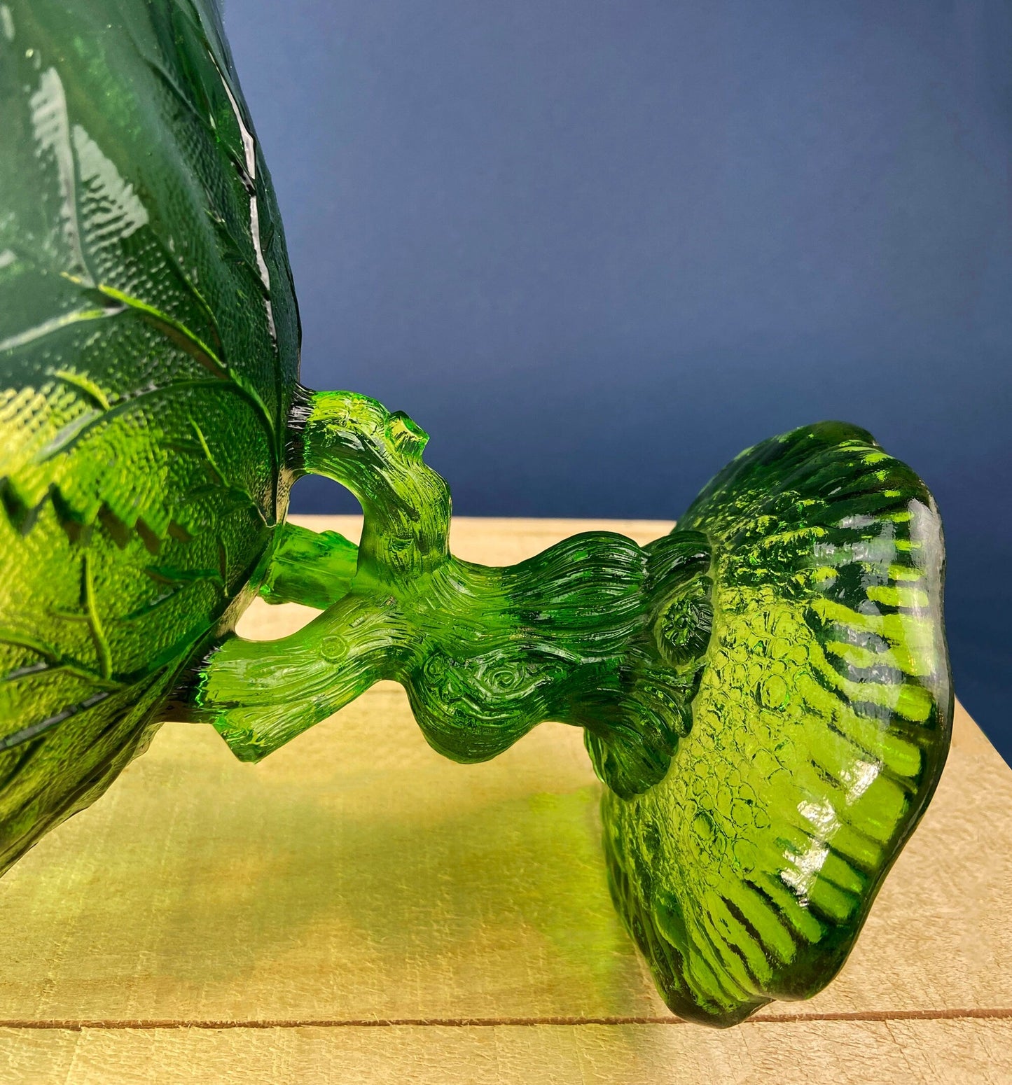 Green glass leaf-shaped object on a wooden surface with a blue background