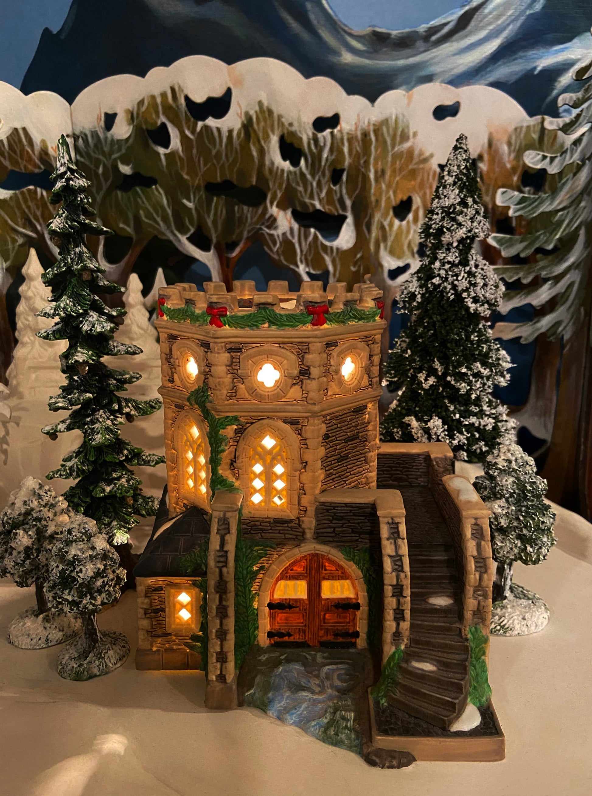 Decorative winter scene with a lit-up castle surrounded by snow-covered trees.