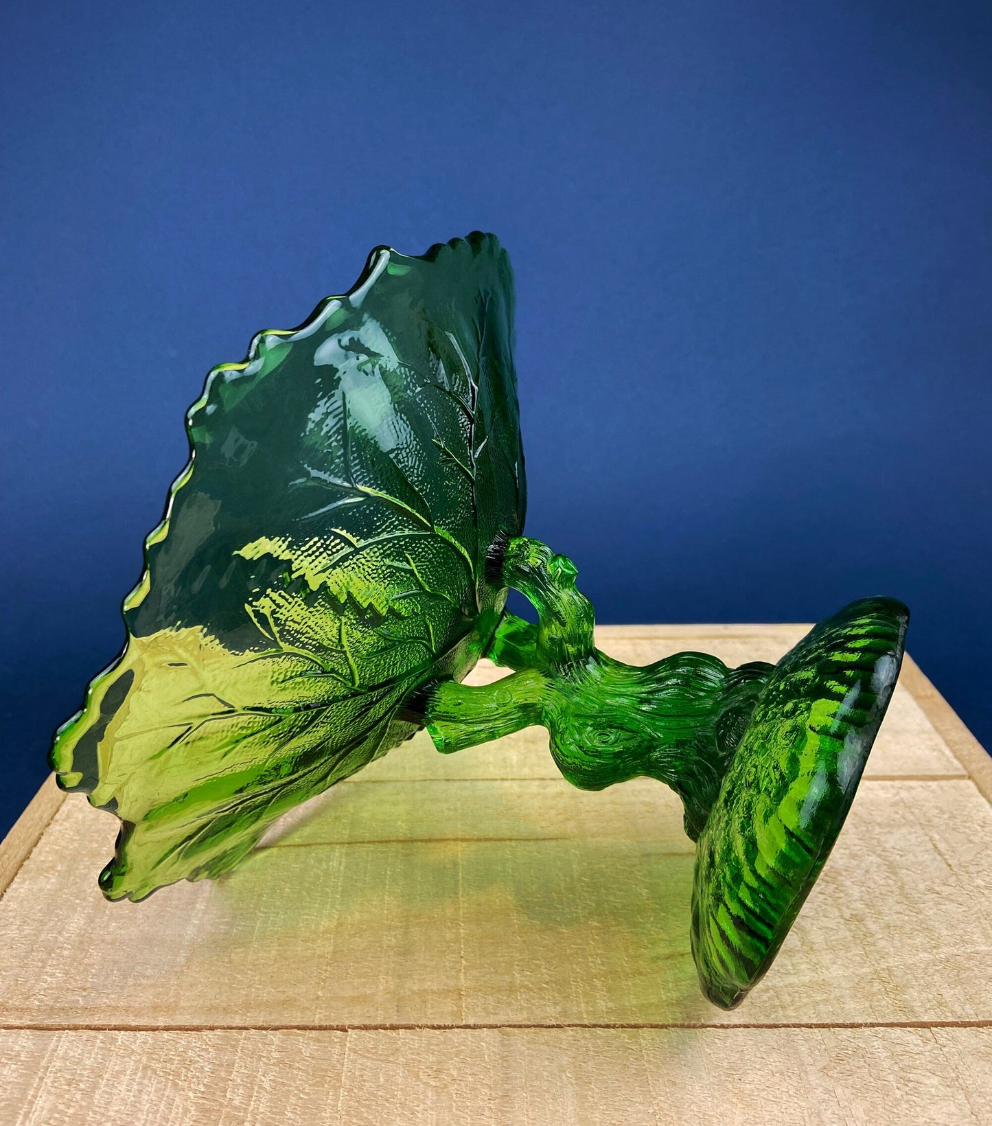 Green glass leaf dish on a wooden surface with a blue background
