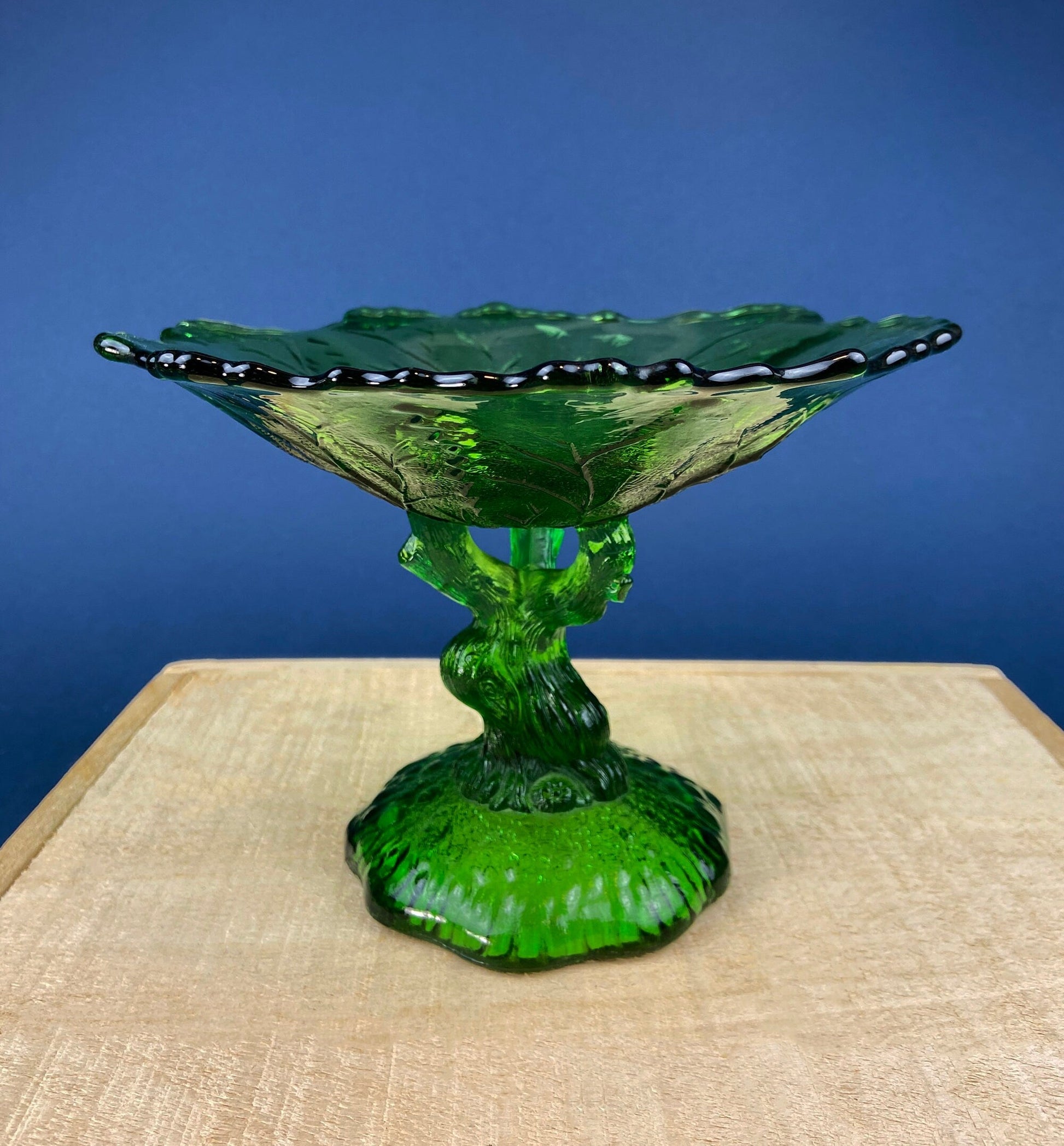 Green glass compote on a beige surface with a blue background