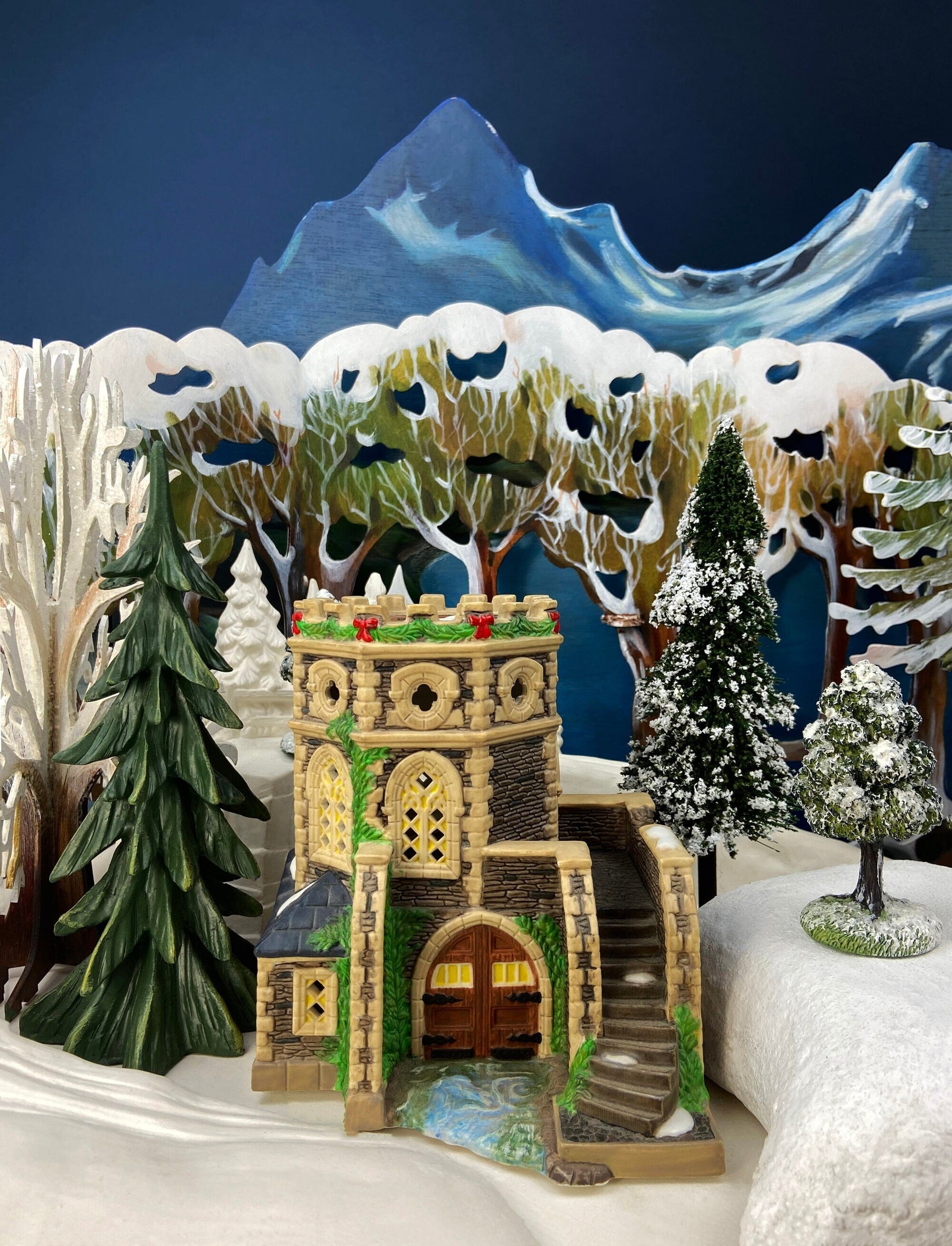 Decorative model of a castle in a snowy landscape with trees and mountains.