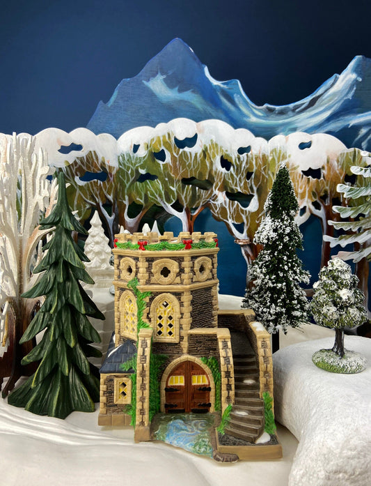 Decorative model of a castle in a snowy landscape with trees and mountains.