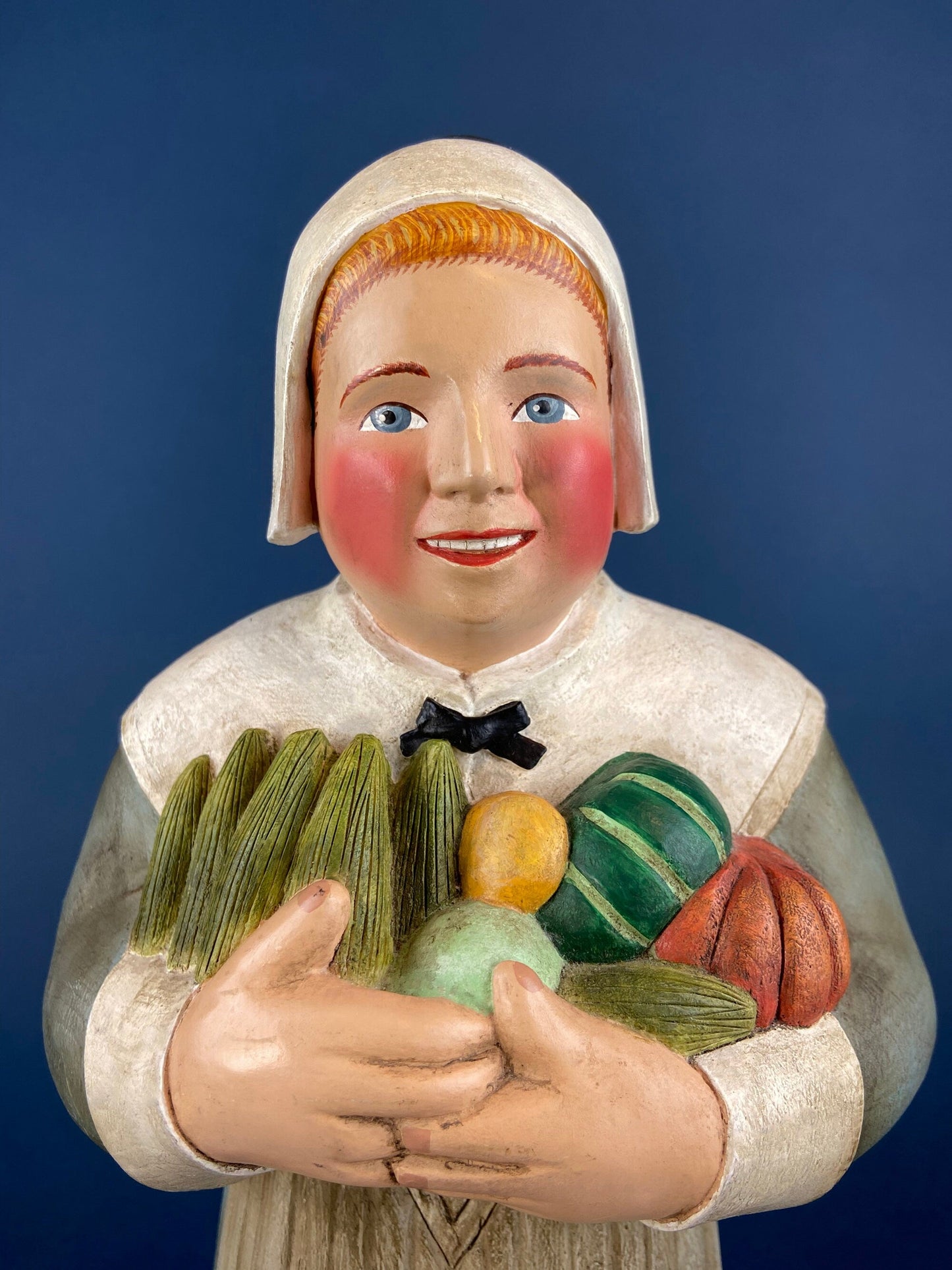 Ceramic figurine of a woman holding vegetables against a blue background