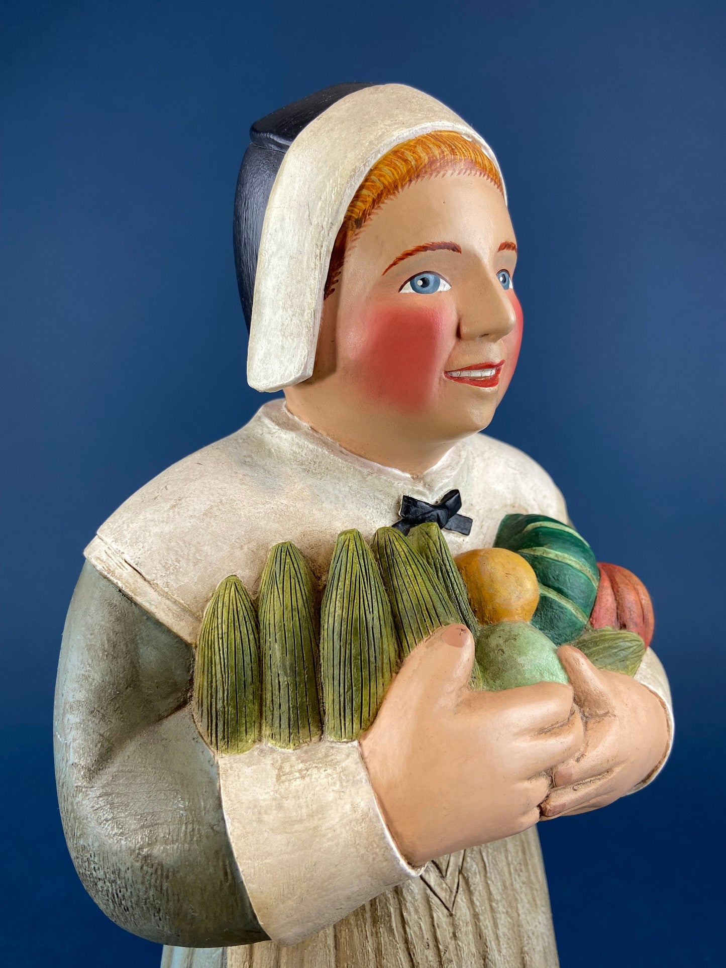 Decorative figurine of a woman holding vegetables against a blue background