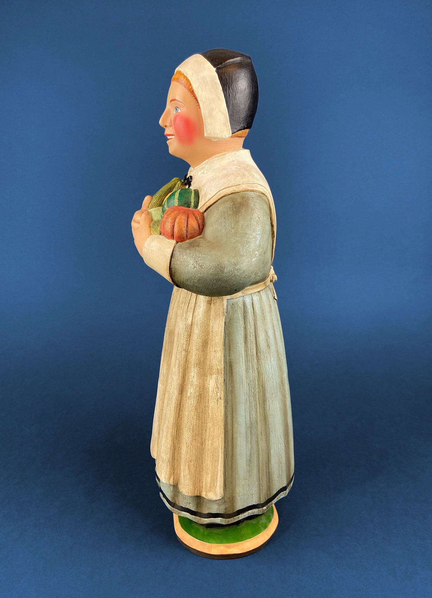 Wooden figurine of a woman holding vegetables against a blue background