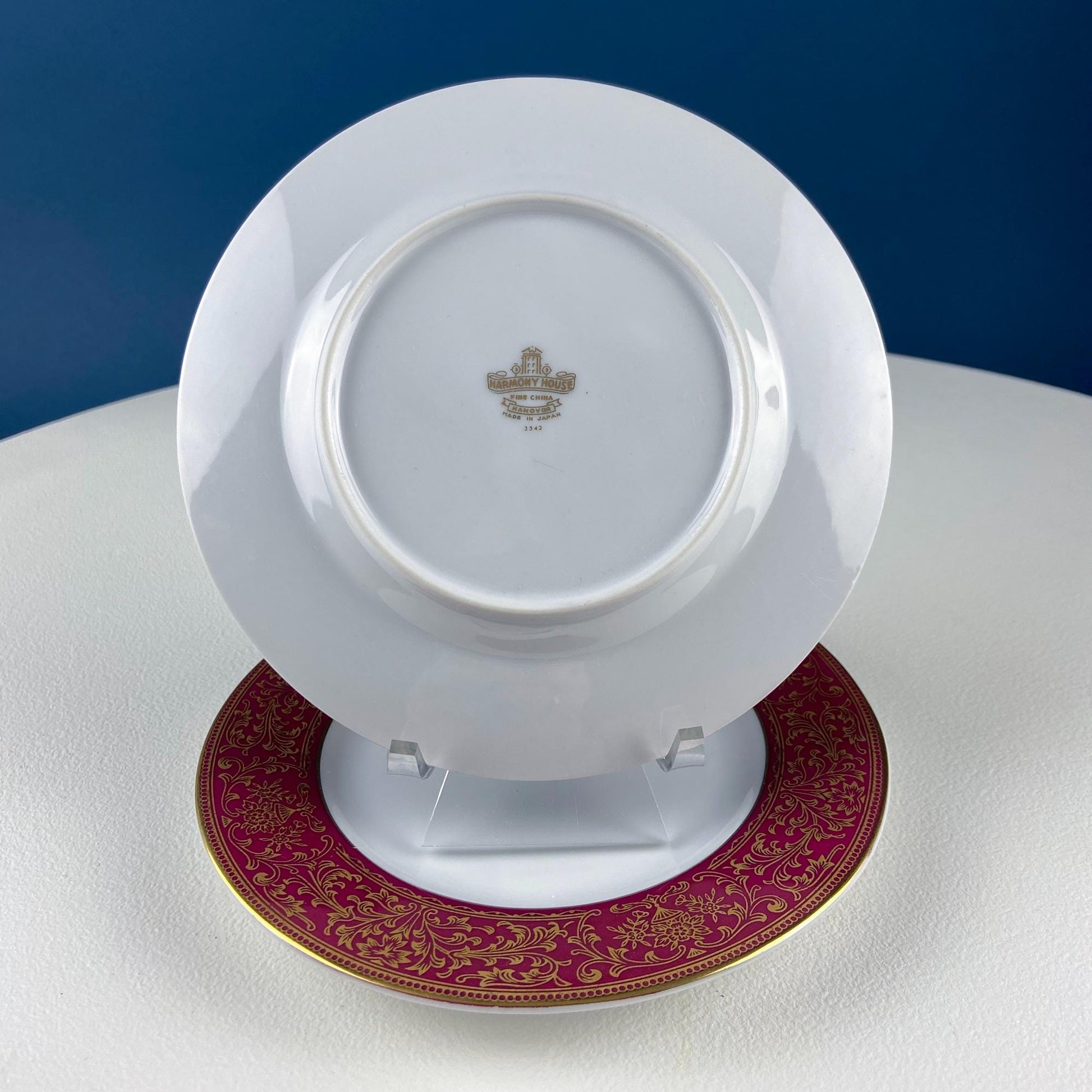 White plate with a gold rim on a white stand against a blue background