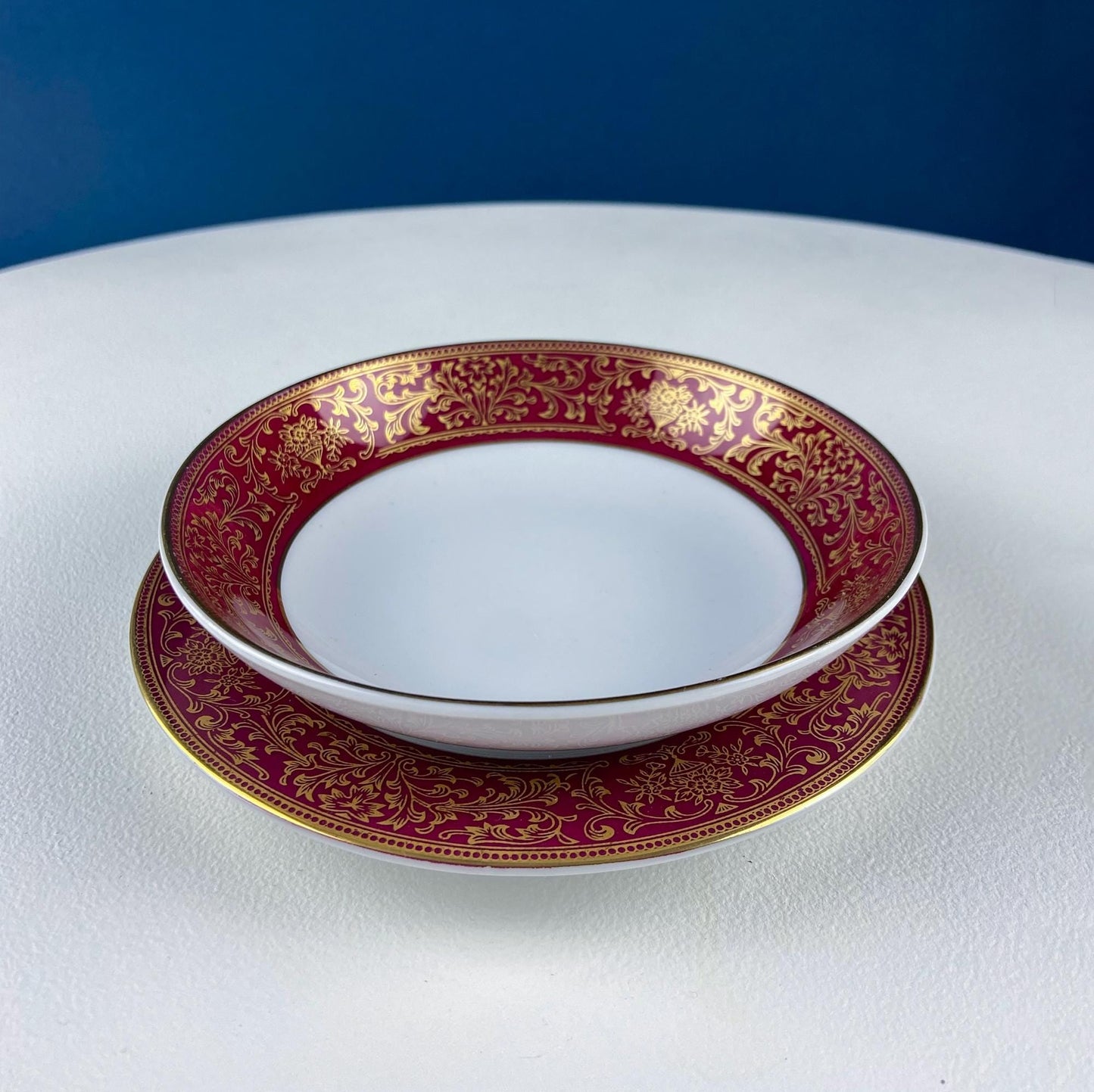 White bowl and plate with red and gold decorative rims on a white surface with a blue background.