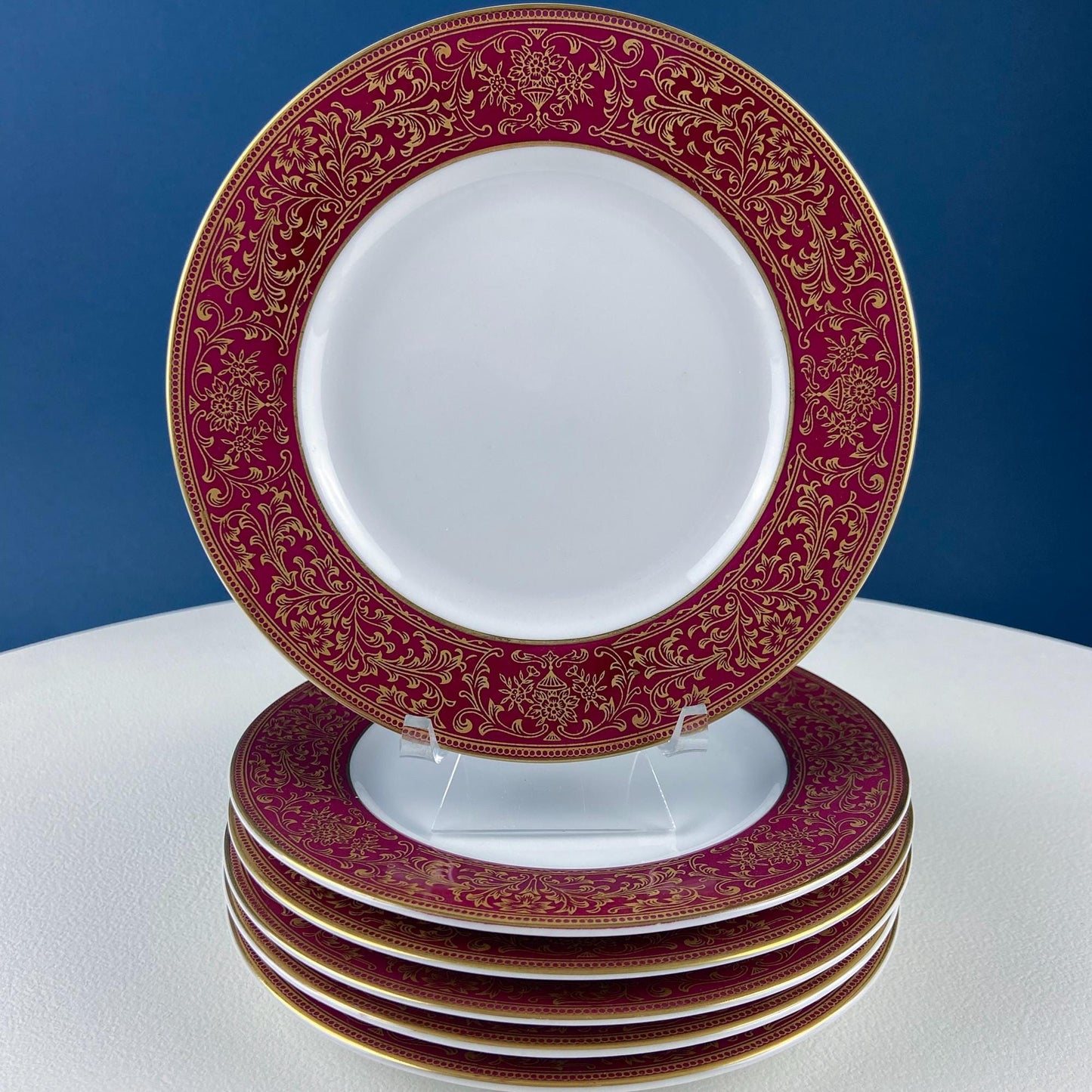 Set of white plates with red and gold decorative rims on a white surface with a blue background