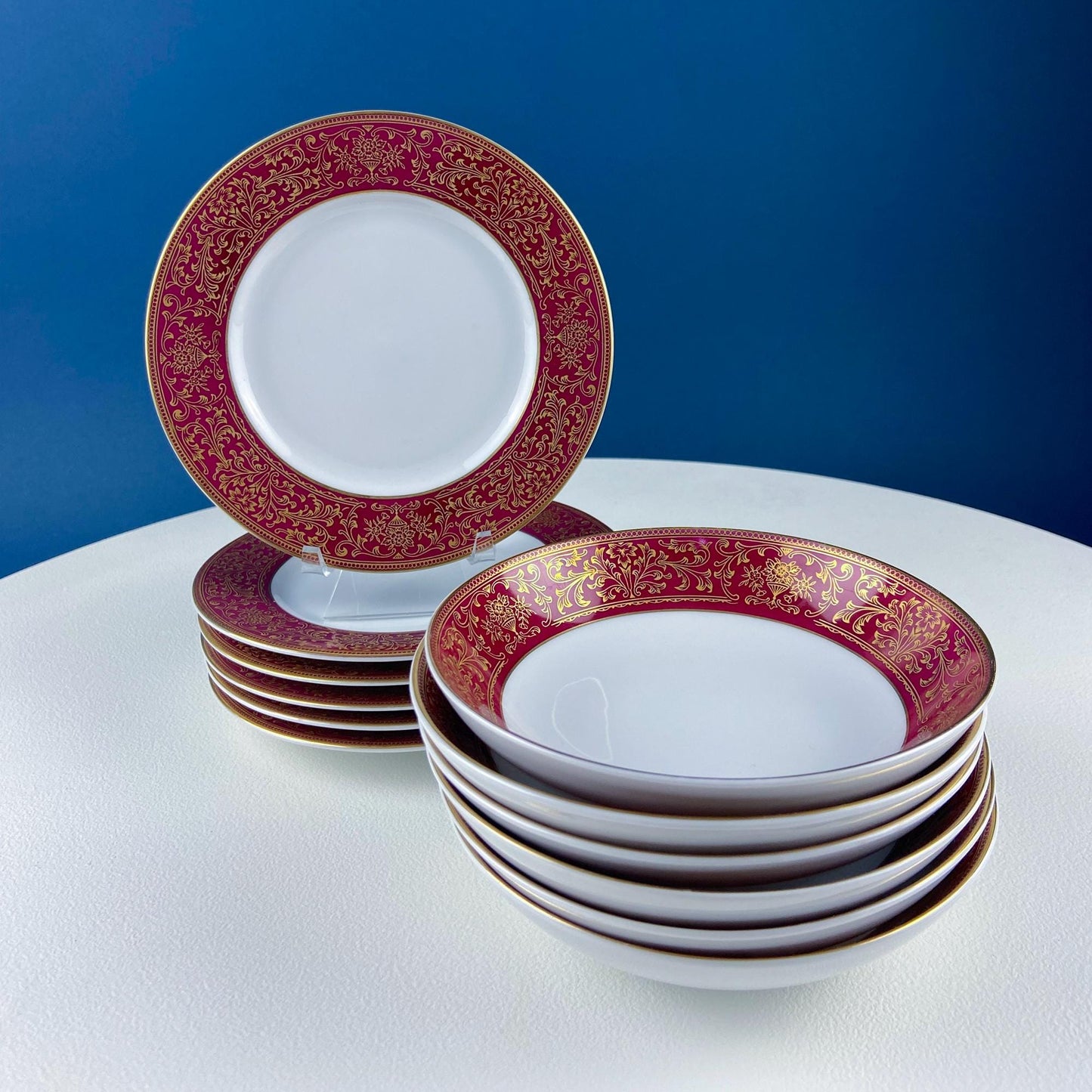 Set of white plates with red and gold rim designs on a white surface with a blue background