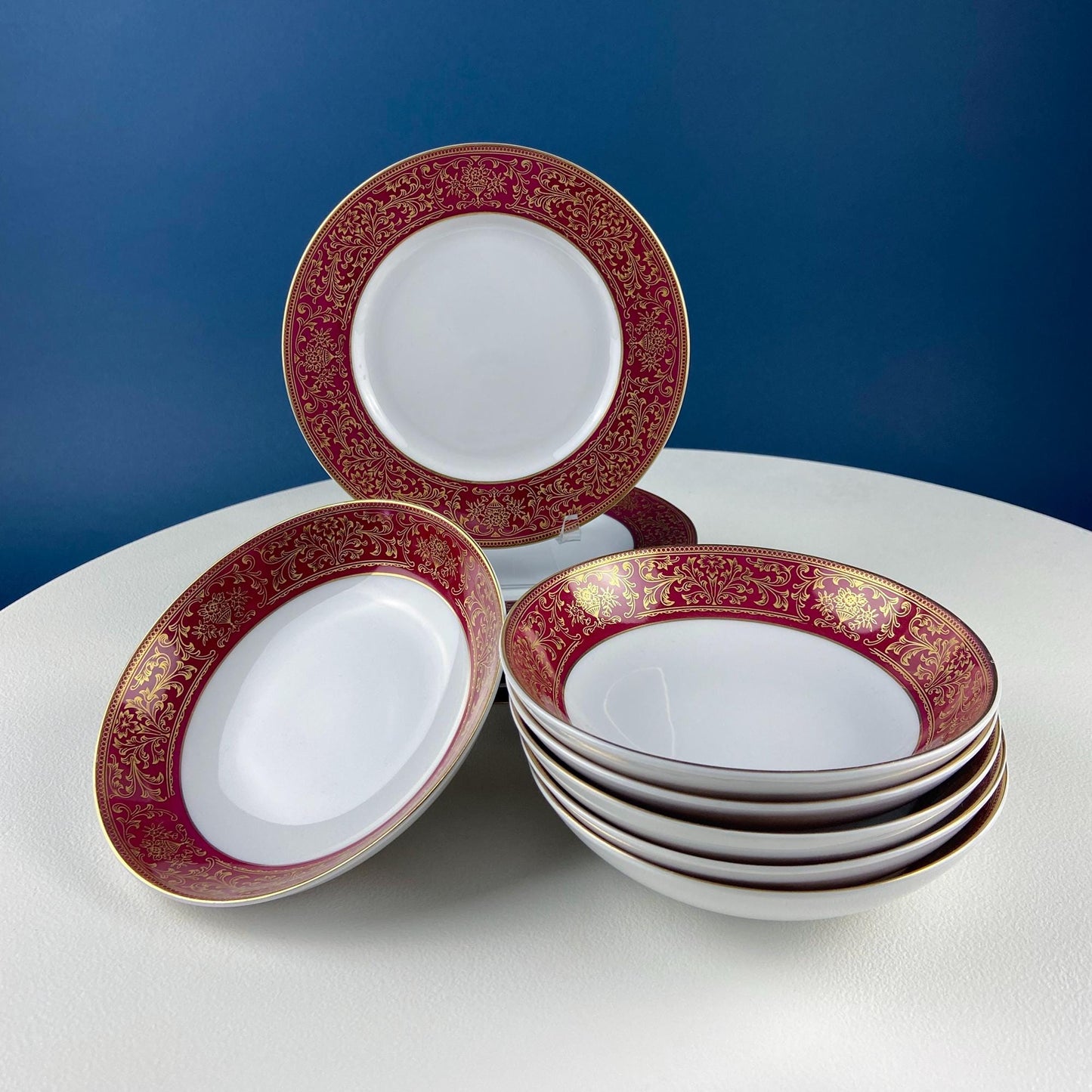 Set of white bowls with red and gold decorative rims on a white surface with a blue background