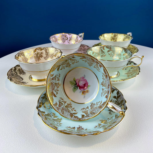 Set of ornate teacups and saucers with floral designs on a white surface.