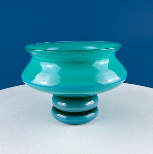 Turquoise glass bowl on a white surface with a blue background