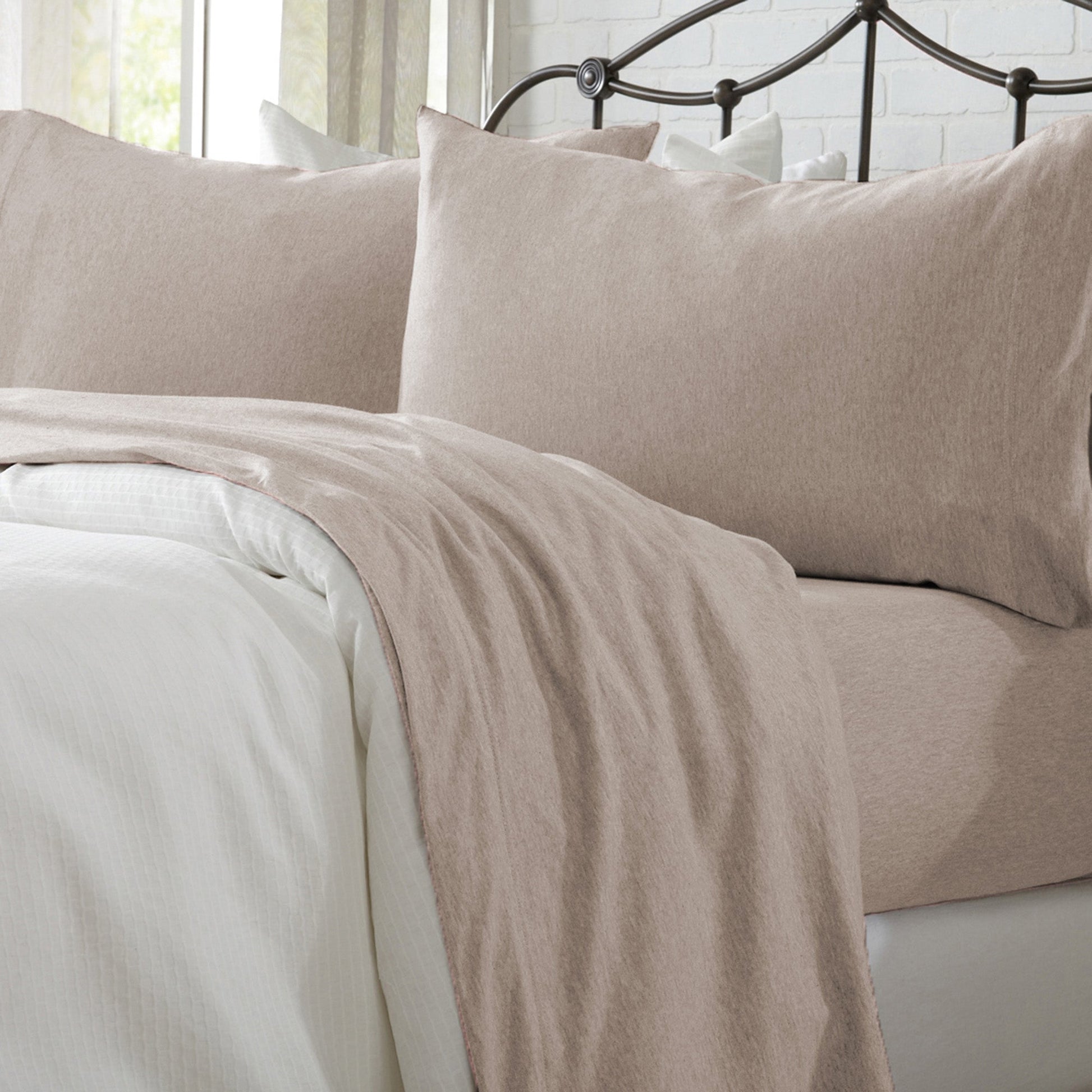 Neatly made bed with beige and white bedding in a well-lit room.