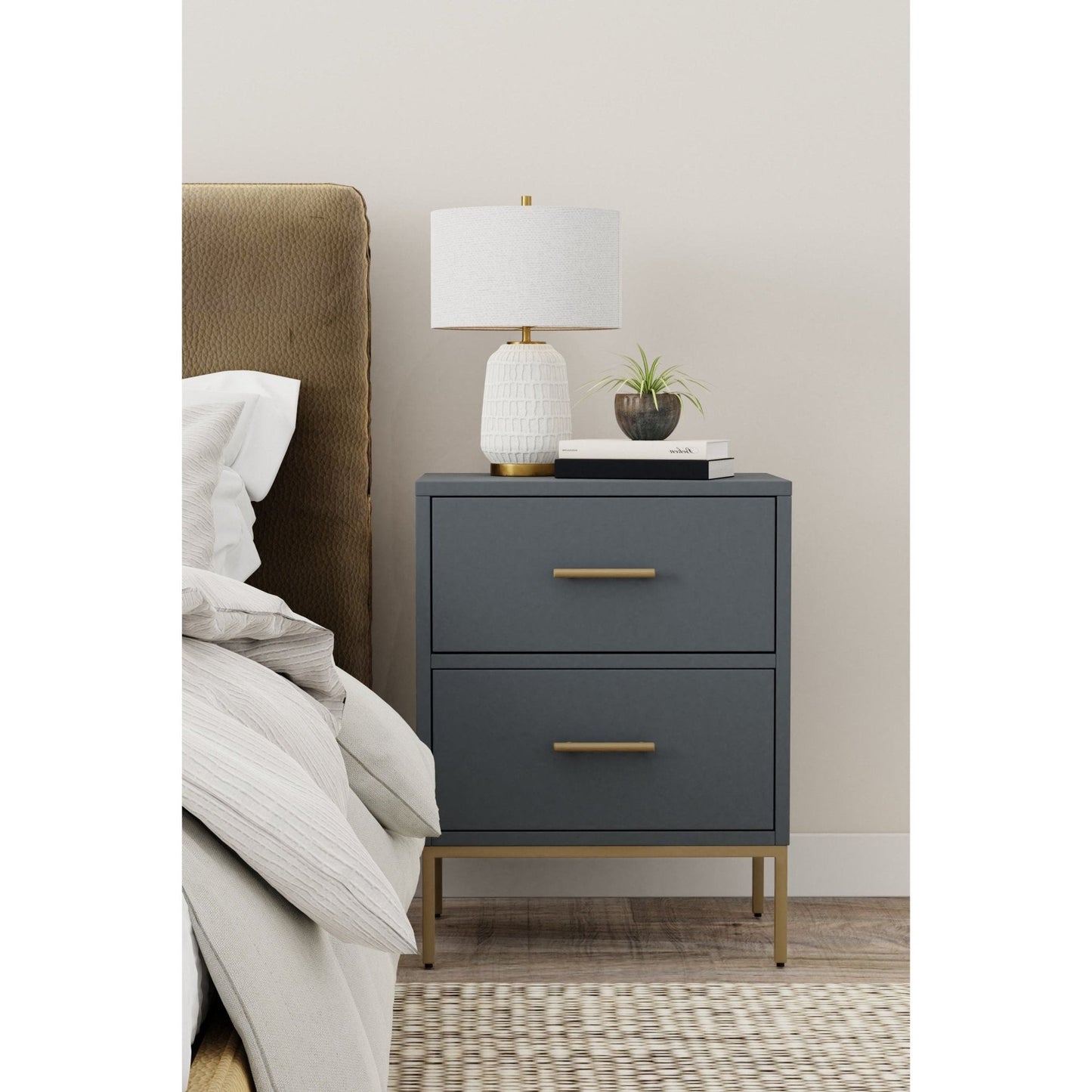 Madelyn Two Drawer Nightstand in Slate Gray with gold hardware, alongside a lamp and decor in a modern bedroom setting.