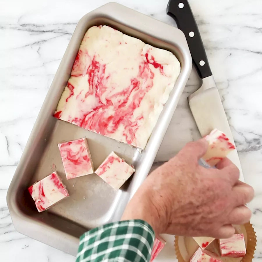 Marble-patterned dessert being cut into pieces on a baking tray with a knife.