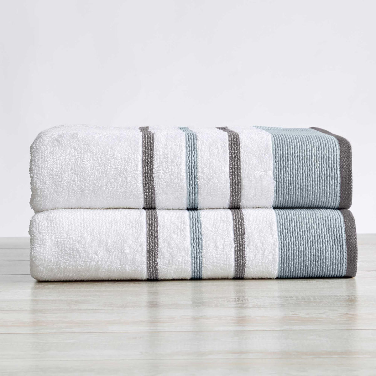 Two folded towels with gray stripes on a light wooden surface and white background