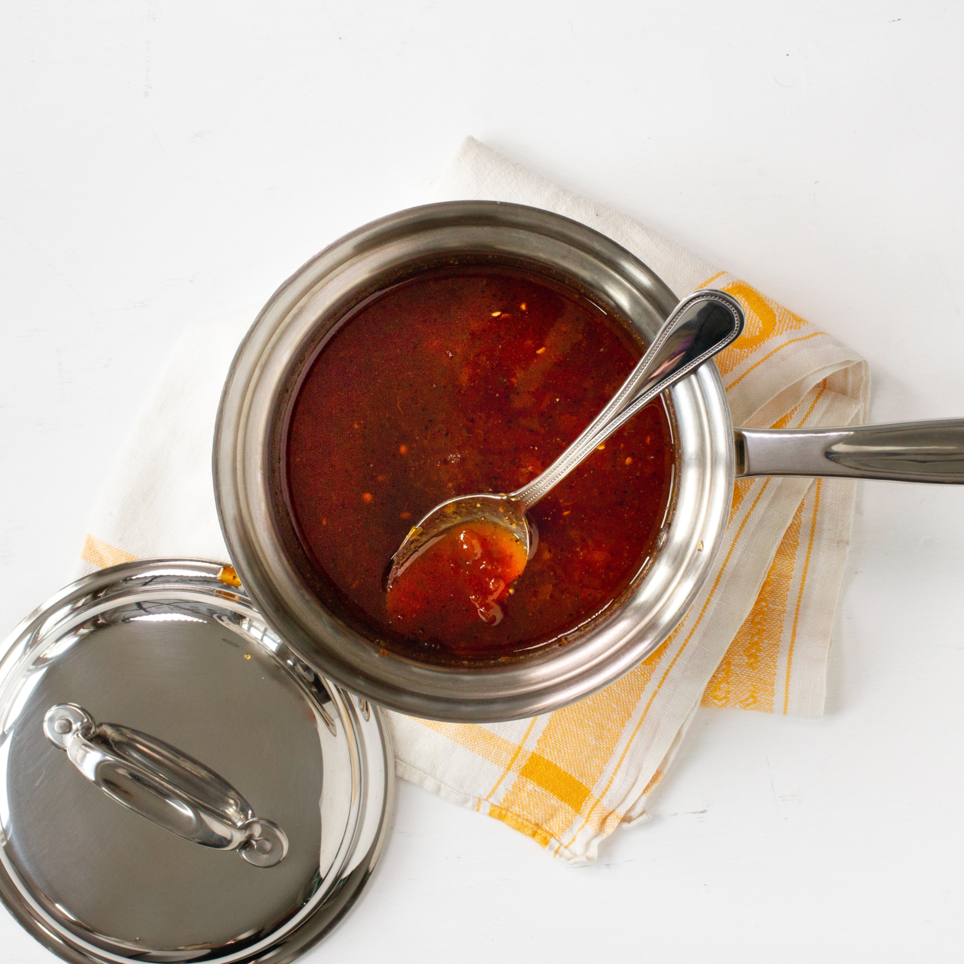 Stainless steel pot with red sauce and a spoon on a white background