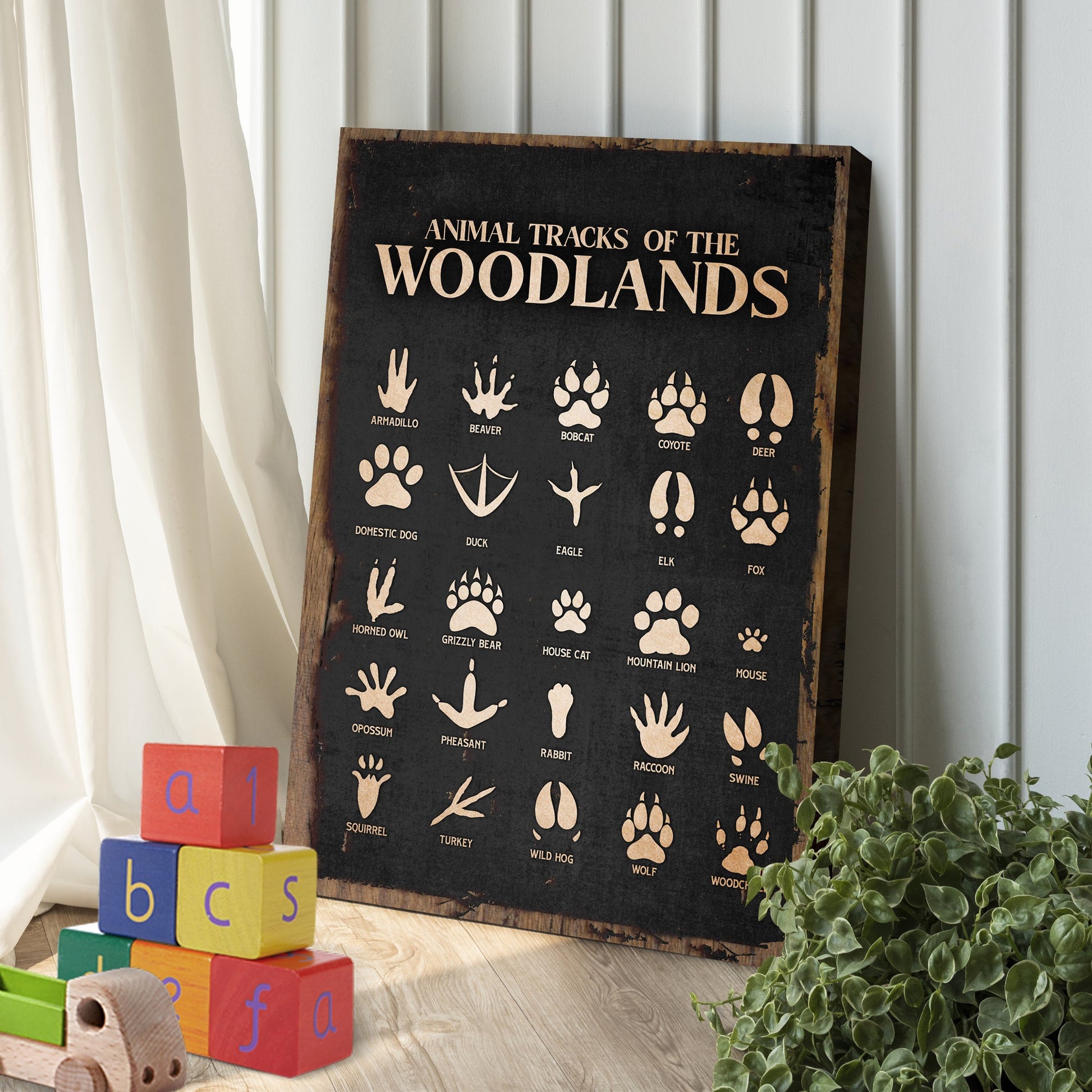 Wooden sign with animal tracks of the Woodlands on a white wall with colorful blocks and a plant.