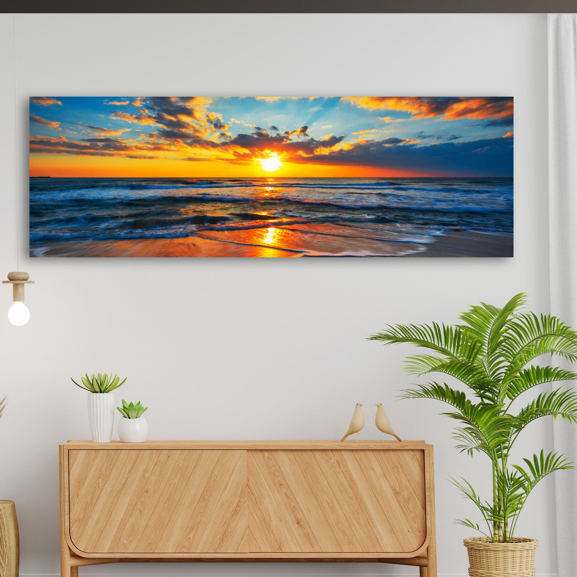 Panoramic sunset over ocean painting on a wall above a wooden console table with plants.