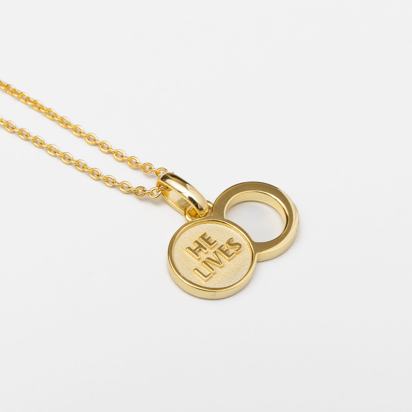 The Empty Tomb Pendant Necklace featuring a gold charm with the inscription 'He Lives'.