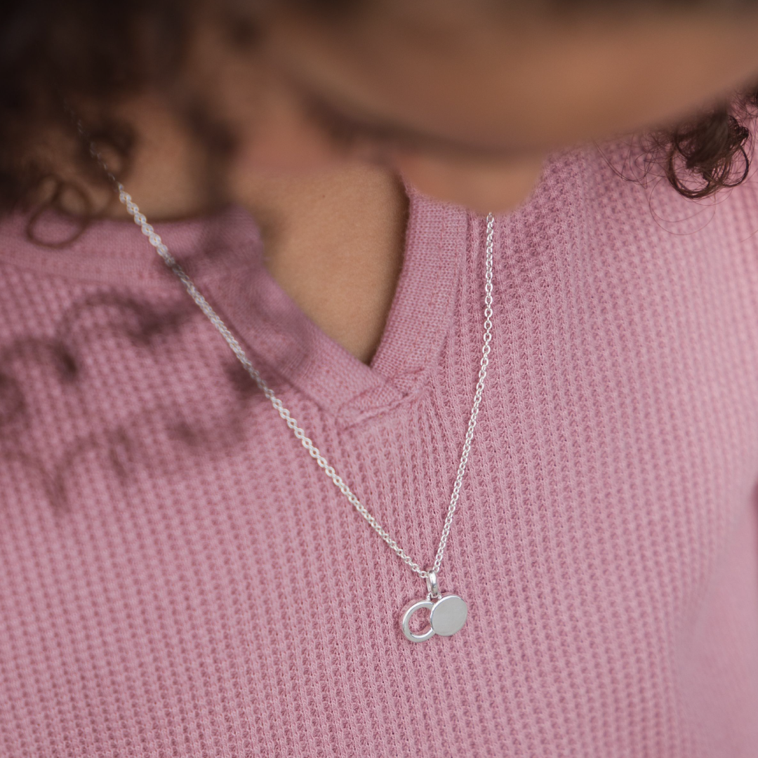 A close-up of a person wearing The Empty Tomb Pendant Necklace, highlighting its two circular charms.