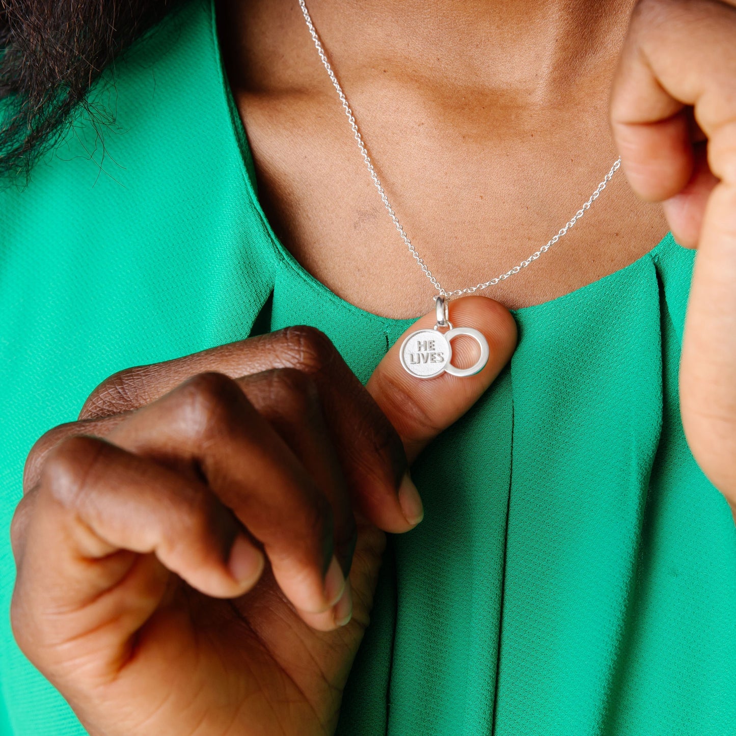 The Empty Tomb Pendant Necklace with the inscription 'He Lives' worn on a stylish green top.