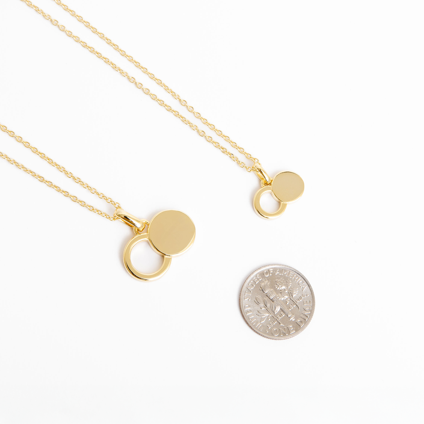 The Empty Tomb Pendant Necklace shown with two gold pendants beside a quarter for size reference.