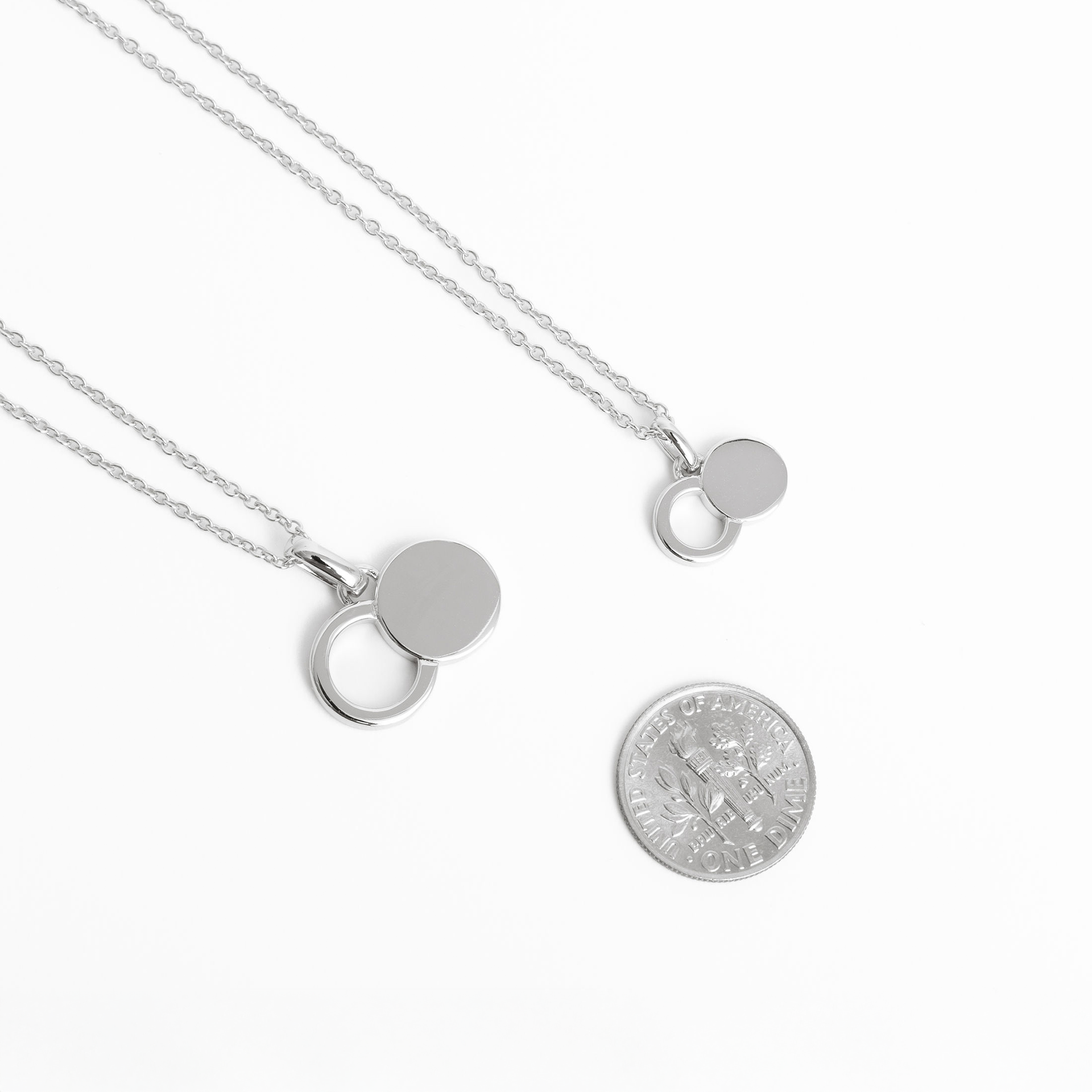 The Empty Tomb Pendant Necklace displayed with a quarter for size comparison, featuring a sleek, modern design.