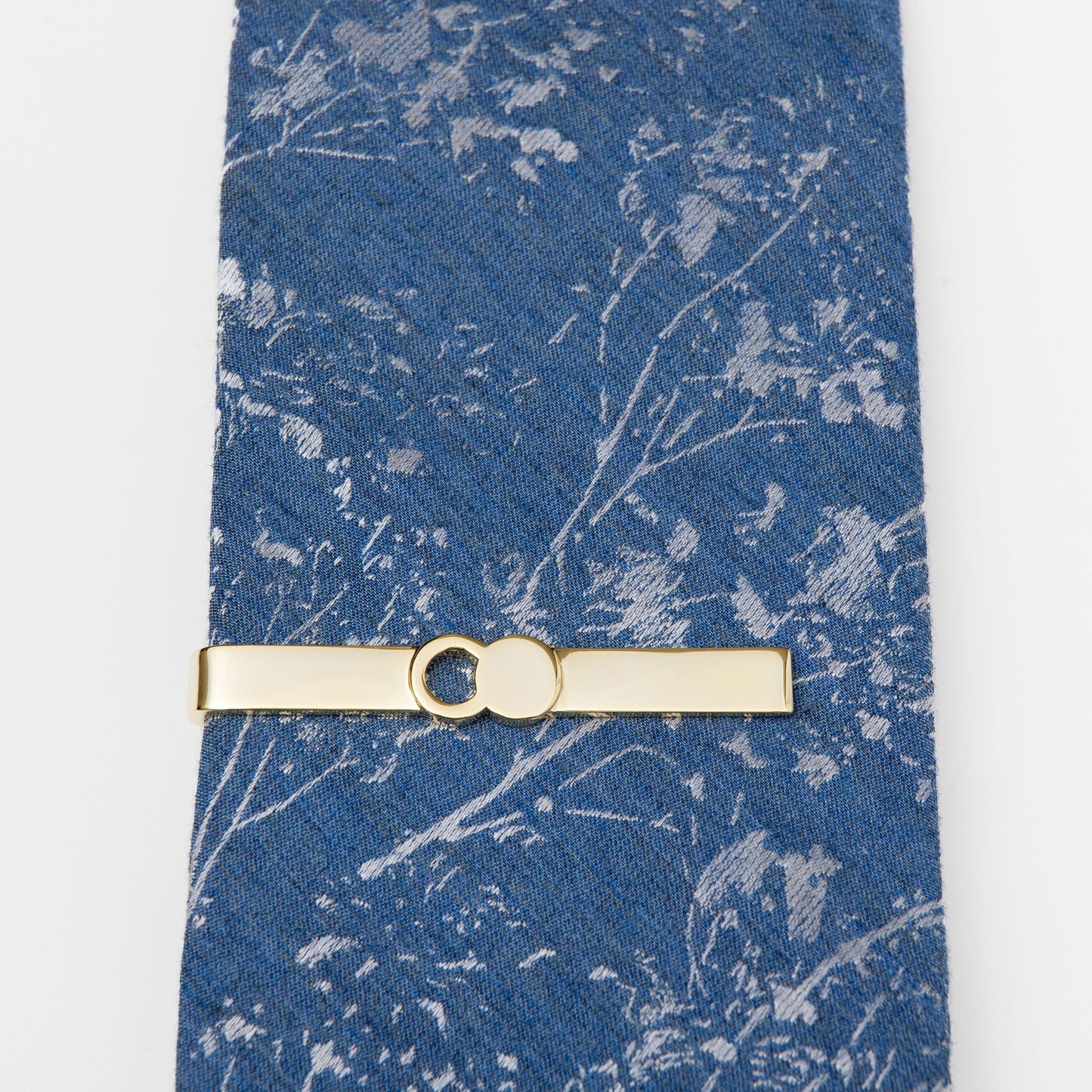 The Empty Tomb Tie Clip displayed on a patterned blue tie, showcasing its sleek brass design.