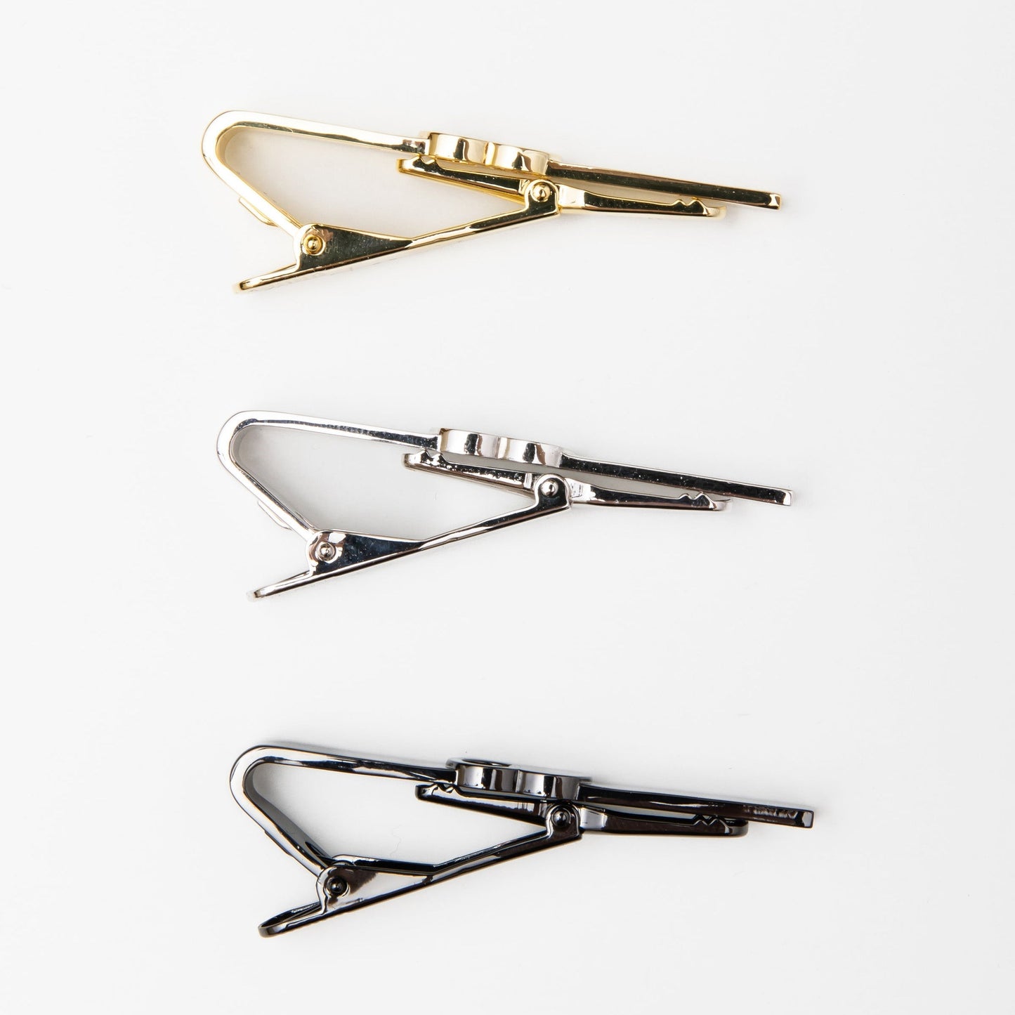 The Empty Tomb Tie Clip in gold, silver, and black finishes displayed on a white background.
