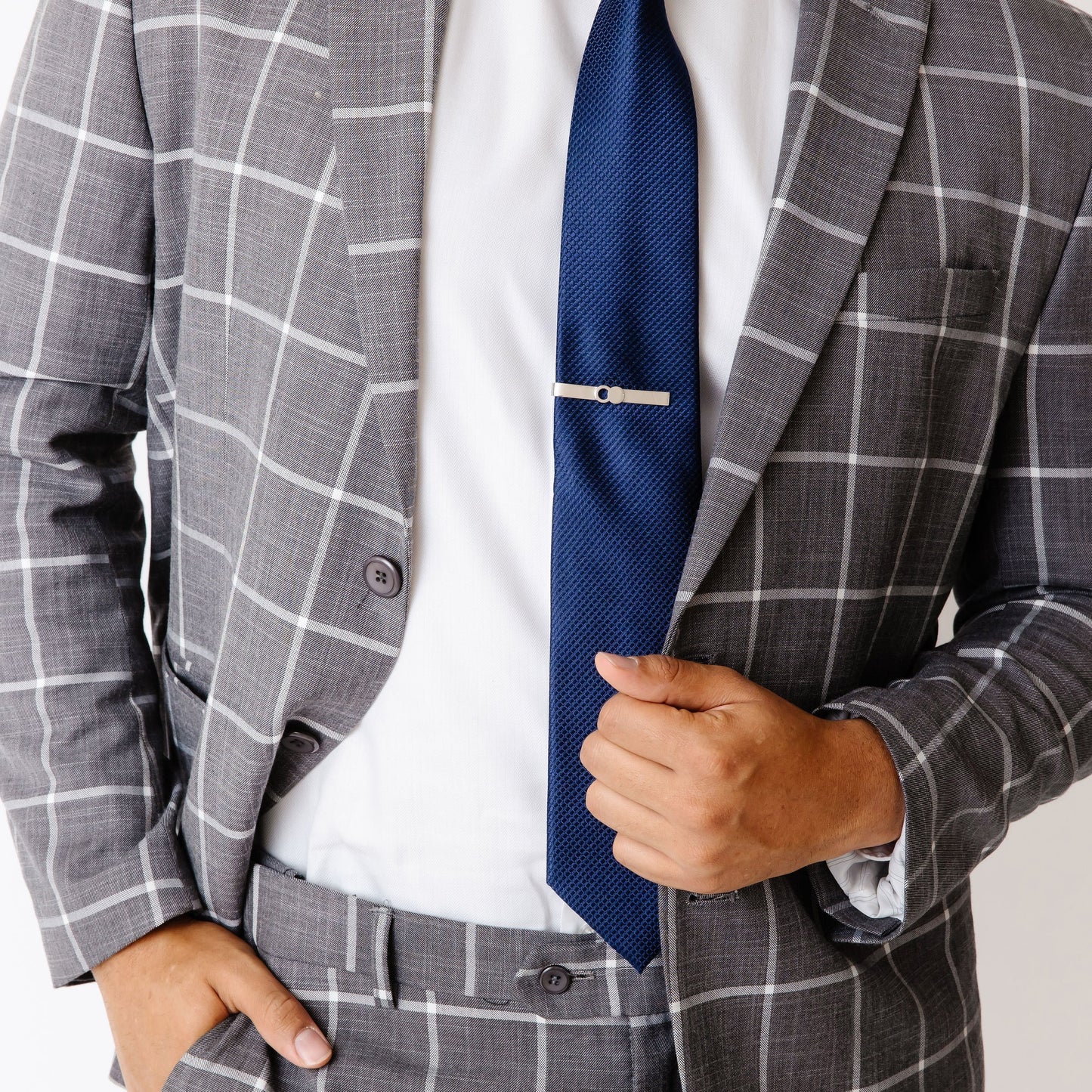 The Empty Tomb Tie Clip displayed on a formal outfit with a gray plaid suit and blue tie.