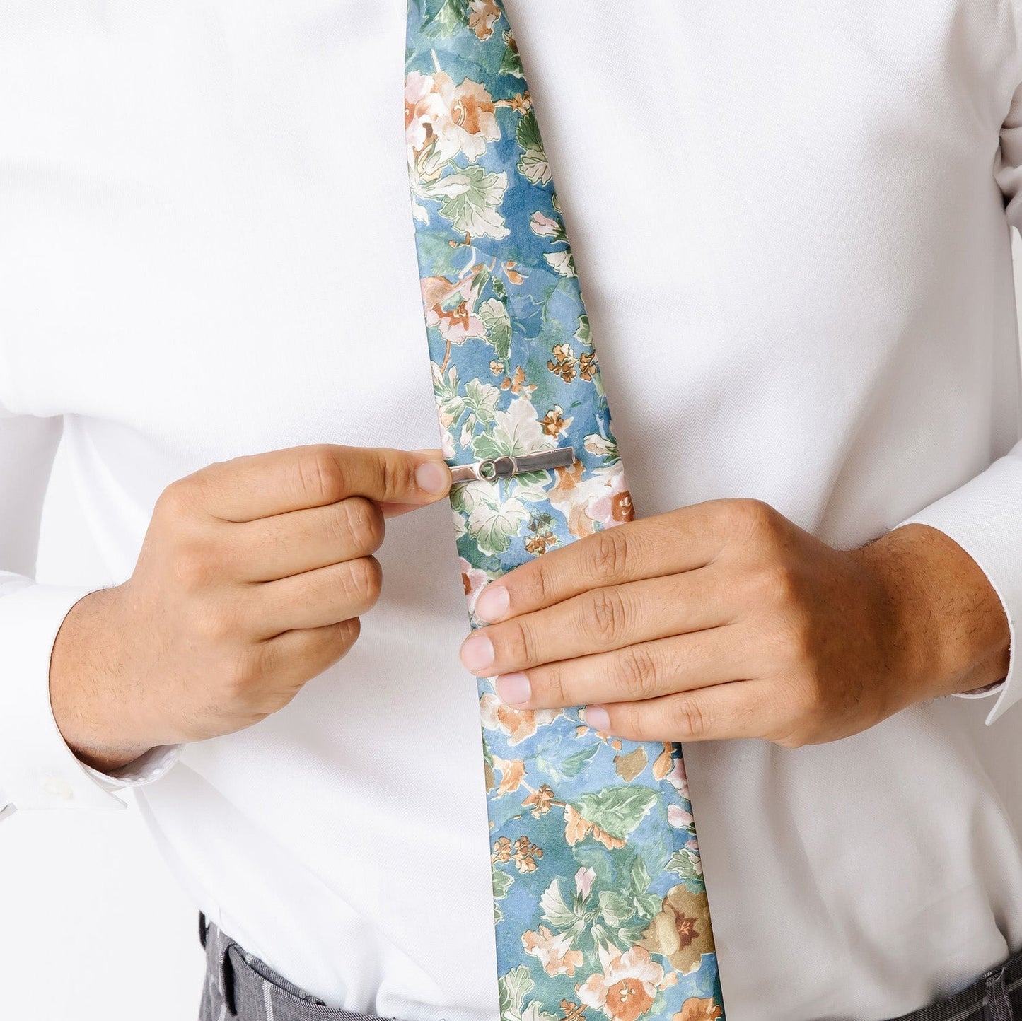 A man adjusting The Empty Tomb Tie Clip on a floral tie.