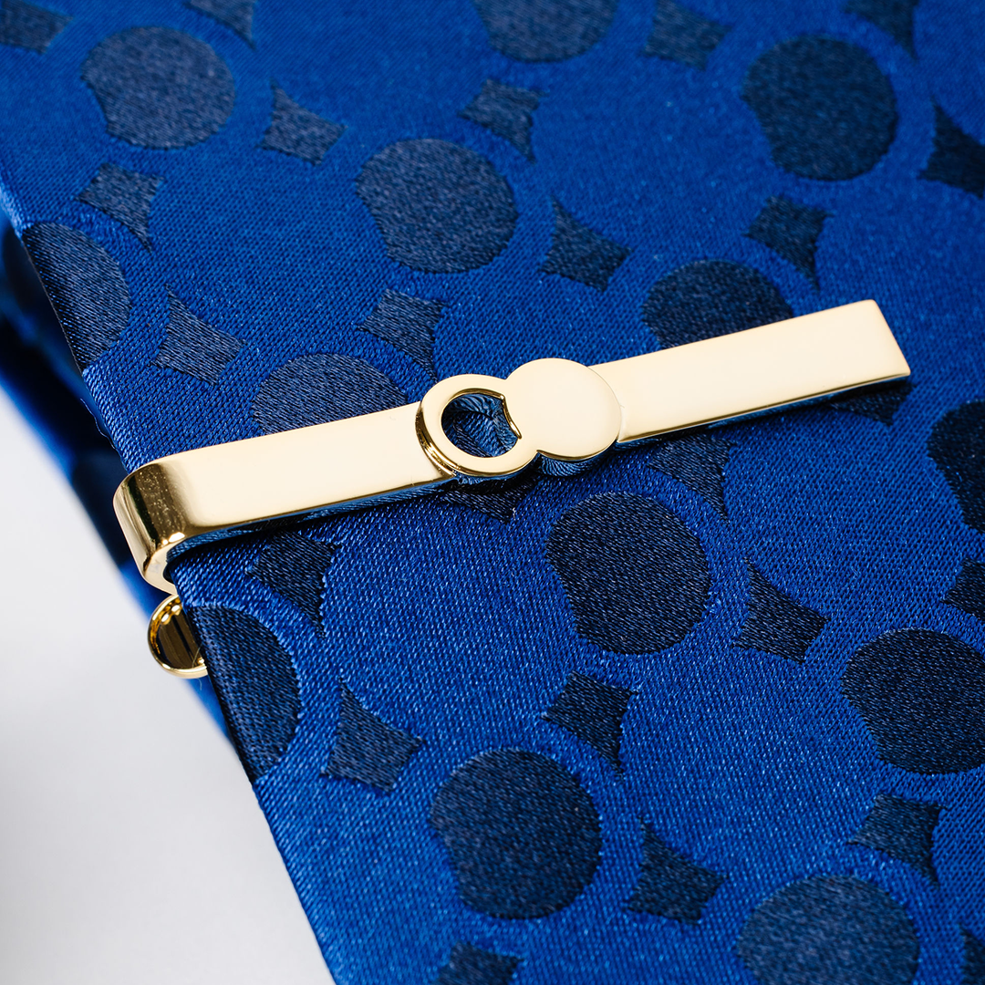 The Empty Tomb Tie Clip displayed on a blue patterned tie, showcasing its sleek brass design and stylish finish.