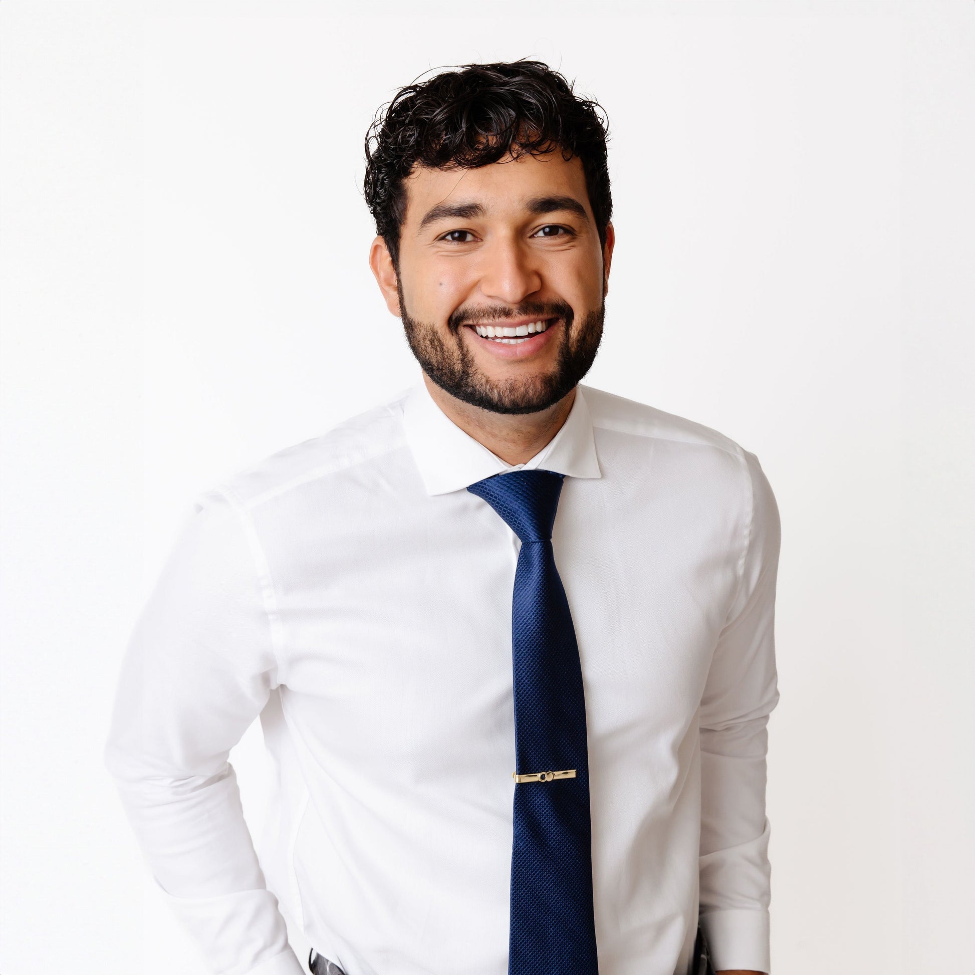 Man in a white shirt and blue tie wearing The Empty Tomb Tie Clip, smiling confidently.
