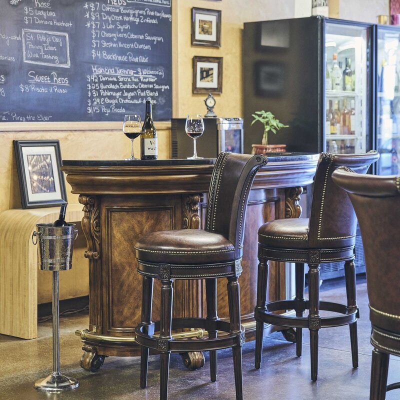Charlotte Swivel Barstool in Distressed Walnut around an elegant bar with wine glasses and a chalkboard menu.