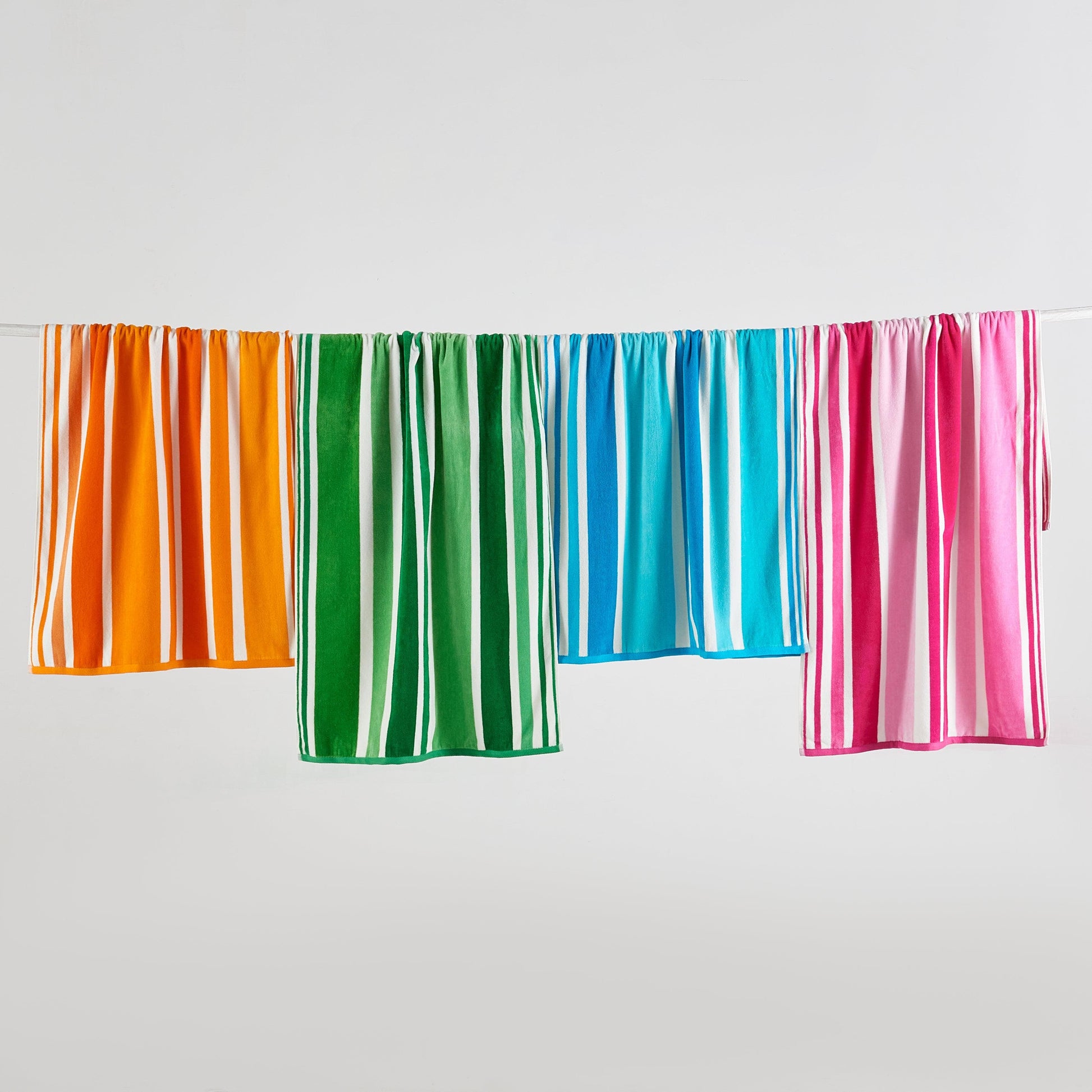 Four colorful striped beach towels hanging on a line against a white background